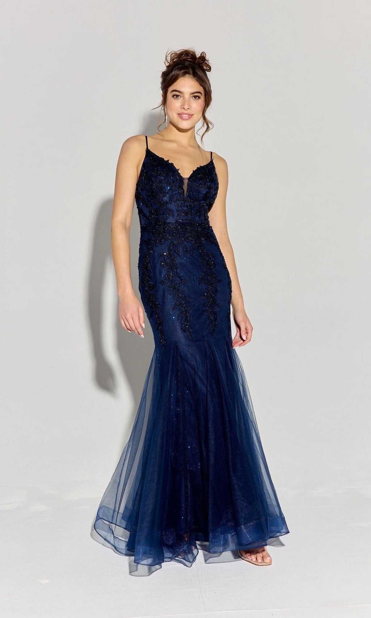 A woman in the Eureka 9998 long prom dress—navy blue, floor-length jersey with lace details, thin straps, and a mermaid godet silhouette—stands against a plain light background.